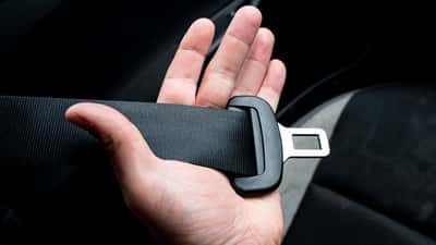A close-up of a hand holding a black car seatbelt across a dark interior.