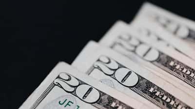 A macro shot of United States twenty-dollar bills neatly layered against a stark black background.