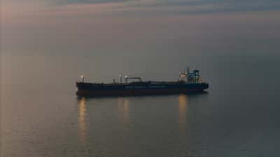 A solitary oil tanker ship sailing on calm ocean waters during twilight.