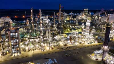 An expansive oil refinery brightly illuminated at night, showcasing the scale of modern energy infrastructure.