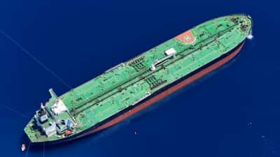 An aerial view of a massive green oil tanker sailing through deep blue ocean waters.