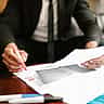 A professional in a suit uses a red marker to review and highlight details on a printed financial document.