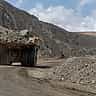 A large yellow mining truck transports rock through a sprawling open-pit quarry.