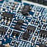 A close-up macro view of a blue electronic circuit board with various surface-mounted components.