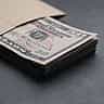 A thick stack of US fifty dollar bills resting partially inside a plain brown envelope on a dark surface.