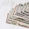 A stack of United States dollar bills rests on a marble surface.