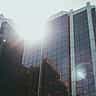Sunlight glares off the grid-like glass facade of a modern commercial office building.