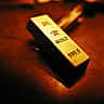 A close-up of a physical gold bar with investment-grade inscriptions under warm lighting.