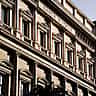 The grand, sunlit neoclassical stone facade of the Banca d'Italia building in Rome.