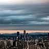 Heavy dark clouds hang over the modern skyline of Seoul at twilight.