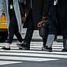 A crop of professionals carrying briefcases as they cross a downtown city street.