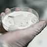 A gloved hand in a laboratory holds a petri dish containing a foamy white substance.