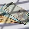 Brazilian real banknotes are displayed in bright sunlight with contrasting diagonal shadows.