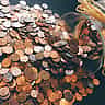 A glass jar lies on its side, spilling a large mound of copper pennies onto a flat surface.