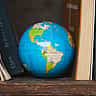 A colorful world globe sits on a wooden bookshelf between classic volumes.