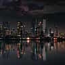The modern high-rises of the Mumbai skyline glow at night, reflecting off the dark waters below.