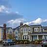 Modern, upscale suburban houses line a residential street under a blue and cloudy sky.