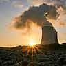 The sun bursts over the horizon in front of two nuclear power plant cooling towers.