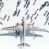 An aerial, top-down view of large military drones on display, surrounded by people casting long shadows on the white ground.
