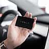 A hand holds a black Tesla key card inside the modern interior of a vehicle.
