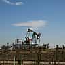 A solitary oil pump jack operates in a dry, sparse landscape under a clear sky.