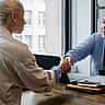 A smiling manager shakes hands with a candidate across a desk in a bright, modern office.