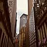 The classic facade of the New York Stock Exchange building stands alongside towering skyscrapers in the dense urban canyon of Wall Street.