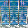 A modern glass ceiling structure looking up toward a bright blue sky.