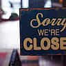 A rustic 'Sorry We're Closed' sign hangs on the glass door of a shop.