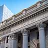 A historic financial building with classical stone columns standing against a clear blue sky.