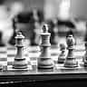 Black and white close-up of wooden chess pieces facing each other on a chessboard.