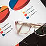 Transparent eyeglasses rest on a printed document displaying colorful pie charts and a legend detailing company allocations.