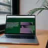 A laptop sits on a wooden desk by a window, displaying the OpenAI website and an introduction to ChatGPT on its screen.