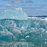 A large, textured blue iceberg floats in the water with its submerged layers visible beneath the surface.