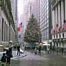 A large decorated Christmas tree stands outside the New York Stock Exchange building during a winter snowfall.