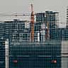 Multiple construction cranes tower over unfinished high-rise buildings surrounded by scaffolding in a Chinese city.