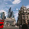 A red double-decker bus passes historic classical buildings and modern glass skyscrapers in the City of London's financial district.