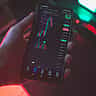 A person's hand holds a smartphone displaying a dark-mode cryptocurrency trading chart with colorful price candles.