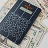 A black digital calculator rests on top of a scattered pile of U.S. dollar bills.