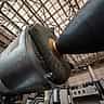 A low-angle view of a massive, metallic rocket booster and its engine nozzle on display inside an expansive aerospace museum.