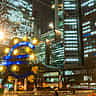 The illuminated Euro sculpture stands in front of office buildings at night in Frankfurt, Germany.