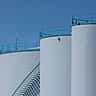 Large industrial white storage tanks stand against a clear blue sky.