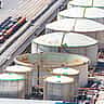 Aerial view of massive white industrial oil storage tanks alongside roads and railway tracks.