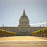 The grand, dome-topped San Francisco City Hall building viewed from a wide, sunlit plaza lined with trees.