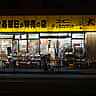 A lone shopper looks at goods outside a brightly lit discount shop in Tokyo at night.