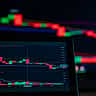 A digital screen displays a cryptocurrency trading chart with prominent red candlestick patterns indicating a market decline.