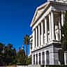 A brightly lit state capitol building with classic white columns against a clear blue sky.