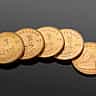 A row of gold Krugerrand coins resting on a dark, reflective surface.
