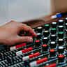 A person's hand adjusts the illuminated knobs and sliders on a professional sound mixing console.