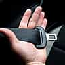 A close-up of a hand holding a black car seatbelt across a dark interior.